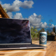 Laptop open on desk next to can of Busch Light, rustic outdoor background